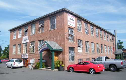 A brick building with multiple windows, a red car parked in front, and a sign for a craft supply store.