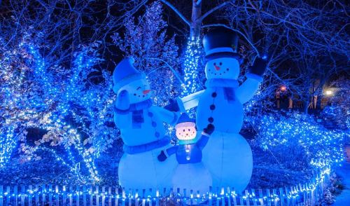 Two large snowmen with blue hats and scarves stand in a winter scene, surrounded by blue holiday lights.