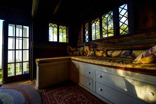 Cozy interior of a room with a window seat, wooden walls, and a door leading outside, illuminated by natural light.