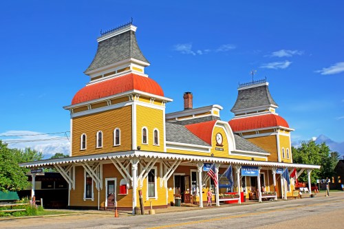 Historic train station with yellow siding, red roofs, and decorative architecture against a clear blue sky.