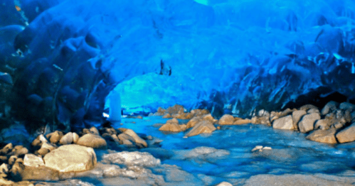 A stunning ice cave with vibrant blue walls and a rocky floor, reflecting light and creating a serene atmosphere.