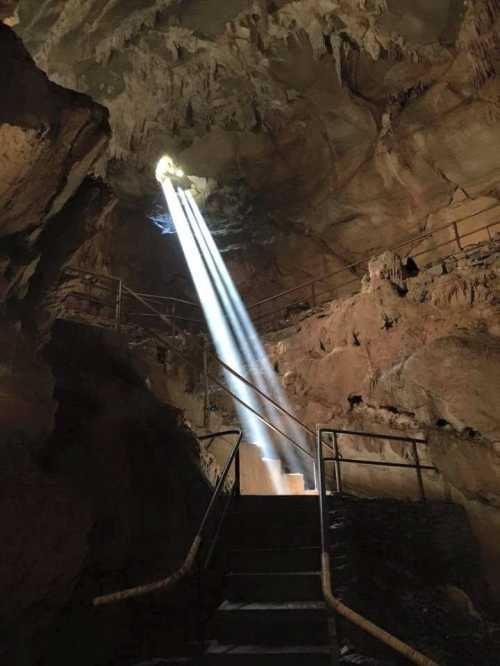 Light beams shine through a cave opening, illuminating stone steps and rocky walls.