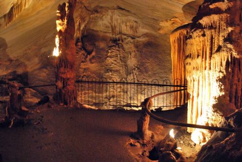 A dimly lit cave interior featuring stalactites and stalagmites, with a winding path and protective railing.