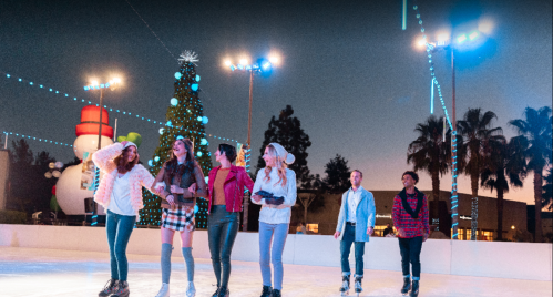 A group of friends ice skating at night, decorated with festive lights and a Christmas tree in the background.