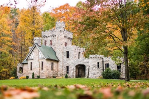 A stone castle surrounded by vibrant autumn foliage and a grassy lawn.