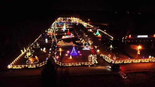 Aerial view of a festive display with colorful holiday lights and decorations along a winding path at night.