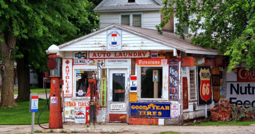 A vintage auto laundry building adorned with colorful signs and gas pumps, surrounded by greenery.