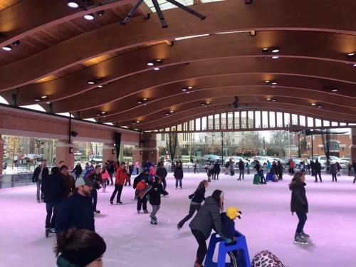 A busy indoor ice skating rink with people skating and enjoying the activity under a wooden ceiling.