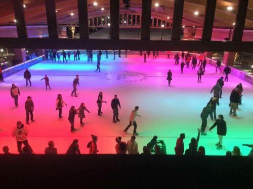 A vibrant ice skating rink filled with people, illuminated by colorful lights in a festive atmosphere.