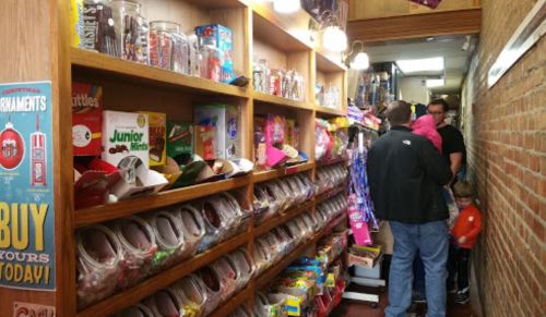 A narrow candy shop aisle filled with colorful candy jars and boxes, with customers browsing and children exploring.