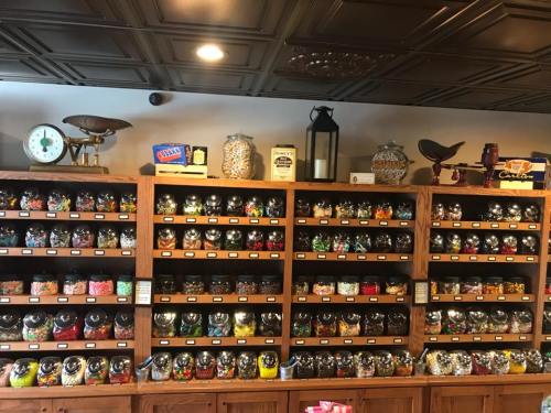 A wooden display shelf filled with various jars of colorful candies and treats, with a vintage clock and lantern above.