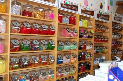 A colorful display of assorted candies in jars on wooden shelves, featuring various shapes and sizes.