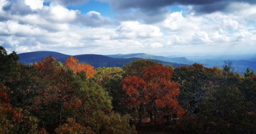 A scenic view of rolling mountains and vibrant autumn foliage under a partly cloudy sky.
