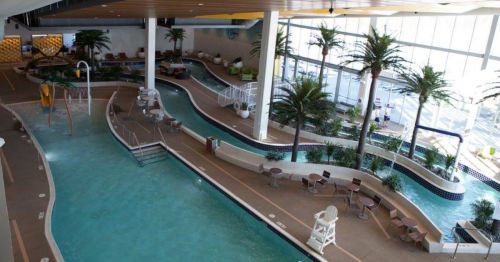 Indoor water park featuring a lazy river, palm trees, and lounge areas with seating. Bright and spacious atmosphere.
