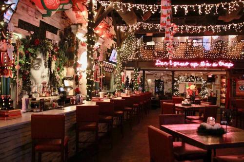 Cozy restaurant decorated with festive lights and holiday decor, featuring a bar and empty tables.