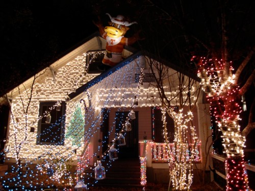 A house decorated with colorful Christmas lights, featuring a large Santa-themed figure on the roof.
