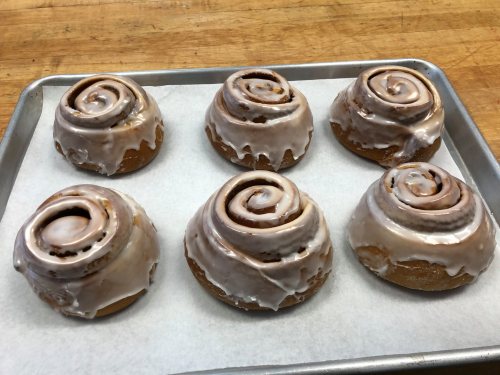 A tray of six freshly baked cinnamon rolls with creamy icing on top, resting on parchment paper.