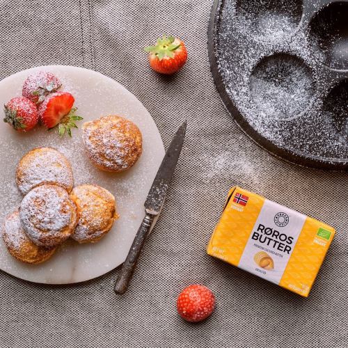 A plate of powdered sugar-dusted pastries with strawberries and a butter package on a textured surface.