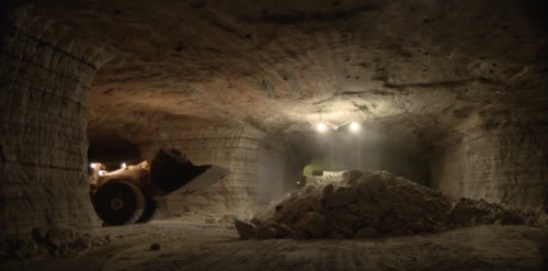 A dimly lit underground mine with a large loader and a pile of material in the foreground.
