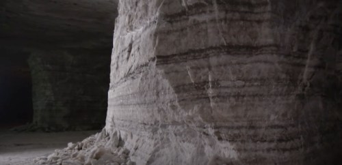 Close-up of a textured salt wall with layered formations in a dimly lit cavern.