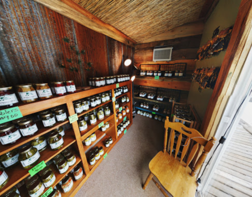 A cozy shop interior with wooden shelves filled with jars of preserves and a chair in the corner.