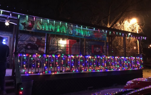 A festive pub exterior adorned with colorful holiday lights and a sign reading "Santa's Pub."
