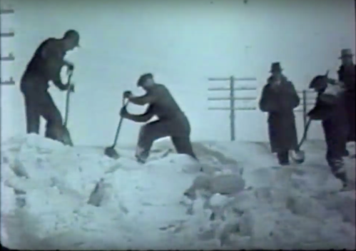 Black and white image of people shoveling snow, with utility poles in the background.