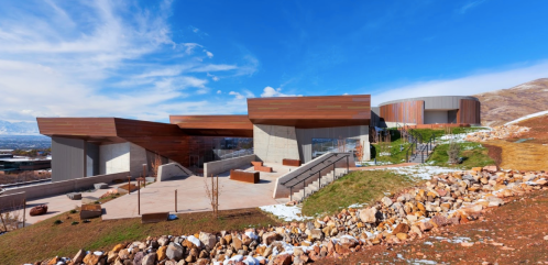 Modern architectural building with wooden and concrete elements, set against a scenic landscape and blue sky.