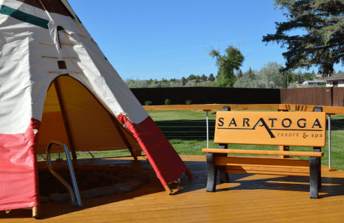 A colorful teepee next to a wooden sign for Saratoga Resort & Spa, set in a green outdoor area.