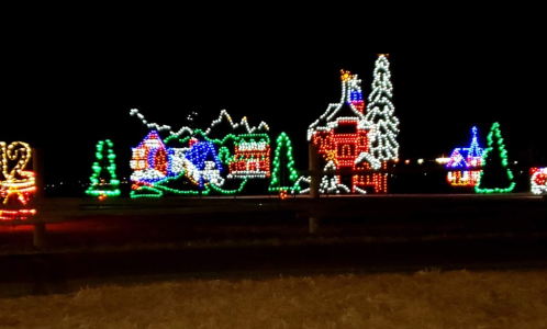 Colorful holiday lights illuminate a festive scene with houses, trees, and mountains against a dark night sky.