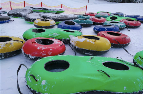 Colorful snow tubes scattered on a snowy slope, with a red safety barrier in the background.