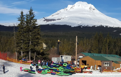 A snowy landscape with people tubing on colorful inflatable tubes, set against a backdrop of a snow-capped mountain.