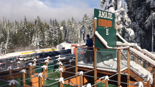 A snowy outdoor amusement area with a large sign reading "AMAZE" and a person standing on a platform.