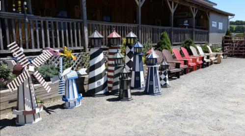 Colorful decorative lighthouses and a windmill displayed outside a rustic building, with chairs arranged nearby.