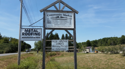 Sign for Community Market with information on metal roofing, fresh homemade donuts, and market hours.