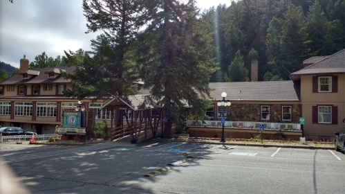 A rustic lodge surrounded by trees, featuring a wooden entrance and a parking area in front.