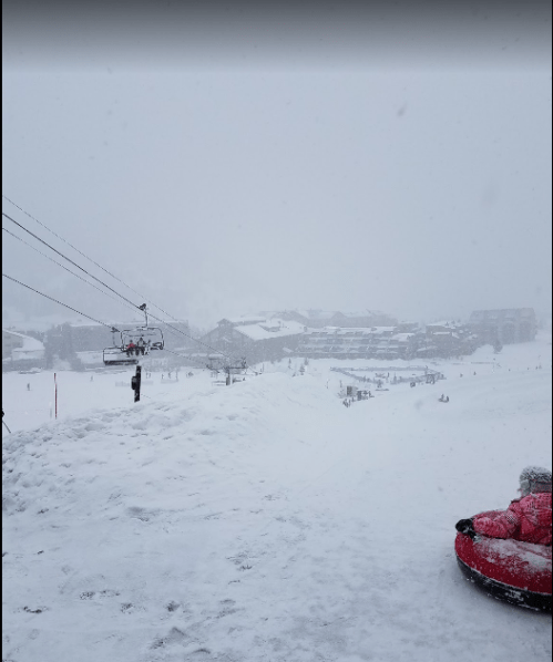 A snowy landscape with ski lifts, a blurred background of buildings, and a red inflatable tube in the foreground.