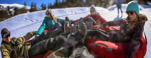 A group of four people enjoying snow tubing on a snowy slope, smiling and wearing winter gear.
