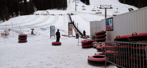 A snowy landscape with people tubing on a slope, surrounded by snow-covered trees and ski lift equipment.