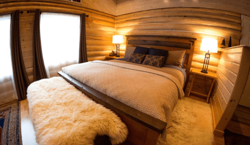 Cozy bedroom with a wooden interior, featuring a large bed, soft rug, and warm lighting from bedside lamps.