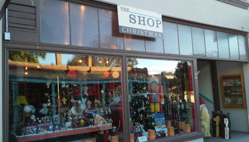 A storefront labeled "The Shop Christmas" featuring festive decorations and a Christmas tree in the window.