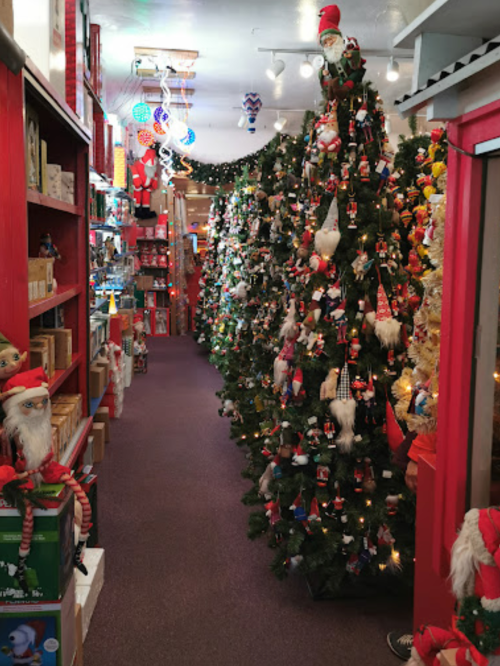 A festive shop aisle lined with decorated Christmas trees and holiday decorations, creating a cheerful atmosphere.
