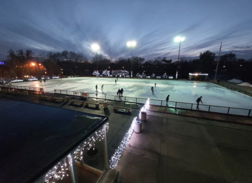 A twilight scene of an outdoor ice rink with skaters gliding on the ice, surrounded by festive lights.
