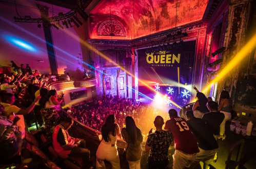 A vibrant concert scene at The Queen in Wilmington, with a lively crowd enjoying colorful lights and performances.