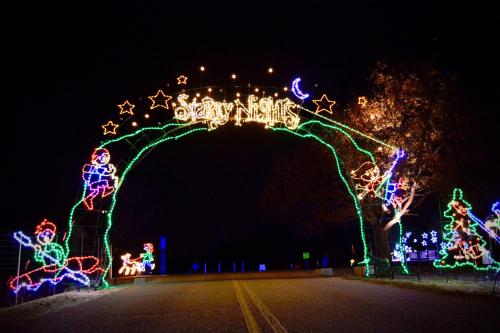 Colorful holiday lights form an archway reading "Starry Nights" over a dark road, with festive decorations on either side.