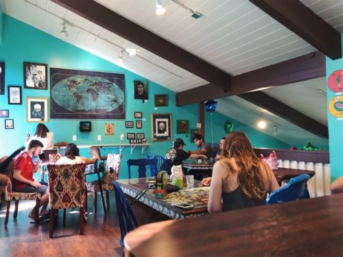 A vibrant café interior with colorful walls, eclectic decor, and people enjoying their time at various tables.