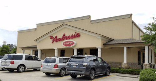 Exterior of Ambrosia Bakery, featuring a beige building with a red sign and parked cars in front.