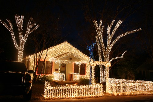 A cozy house adorned with bright white lights, surrounded by illuminated trees and a festive fence at night.
