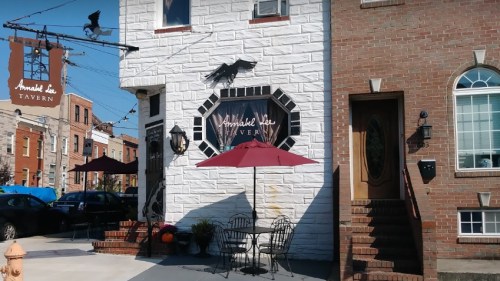 Exterior of Annabelle Tavern featuring a white and brick facade, outdoor seating with a red umbrella, and a sign.