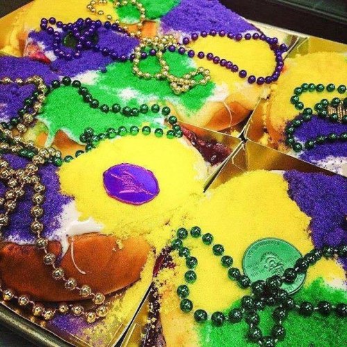 Colorful King Cake decorated with purple, green, and yellow sugar, topped with beads and a coin. Perfect for Mardi Gras!